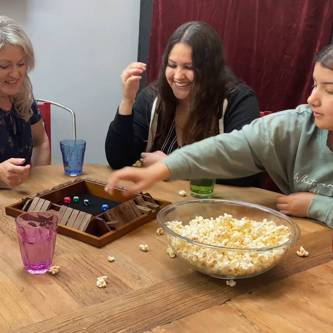 Three people playing a board game with a bowl of popcorn on a wooden table.