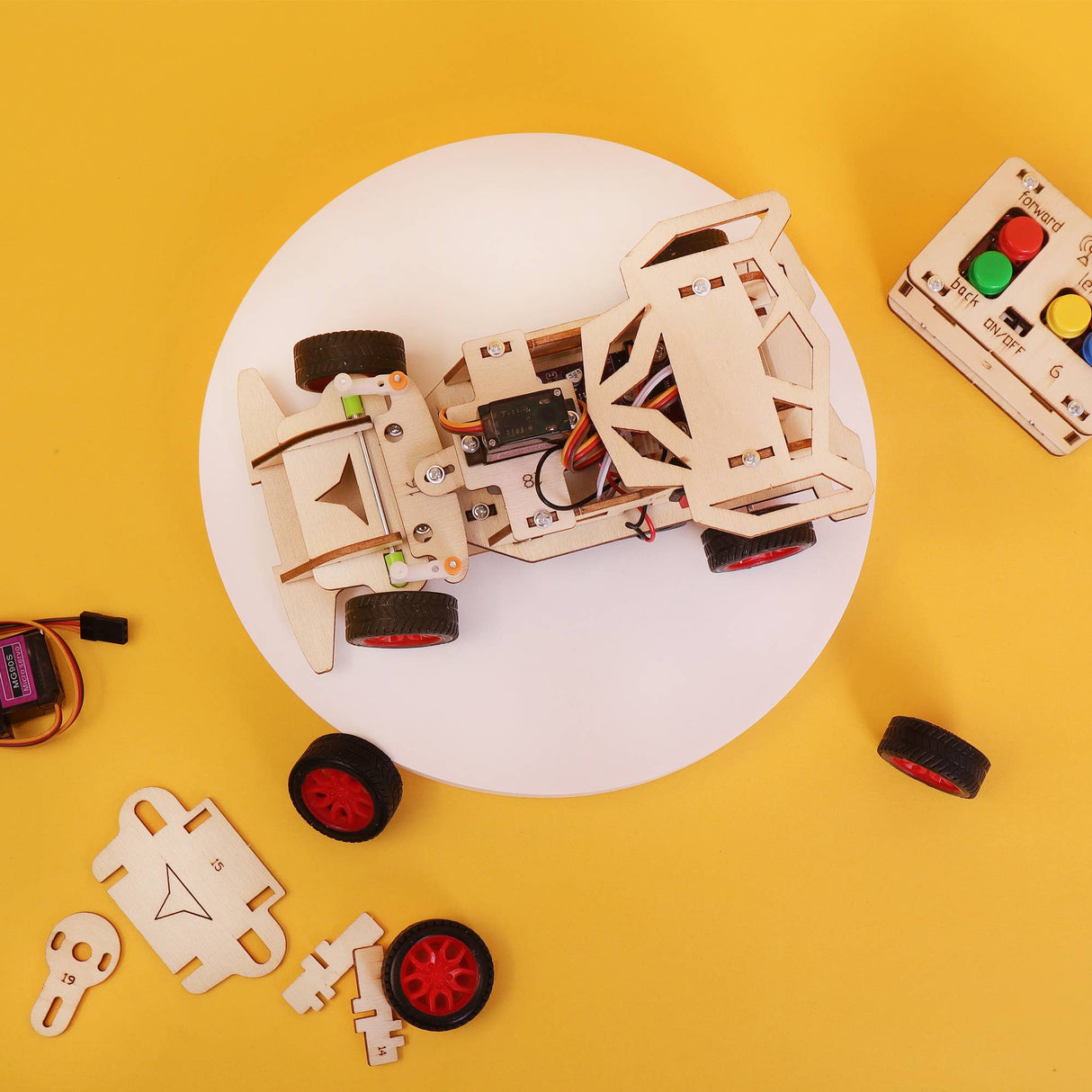 Wooden robot model on a white plate with remote control and parts on a yellow background