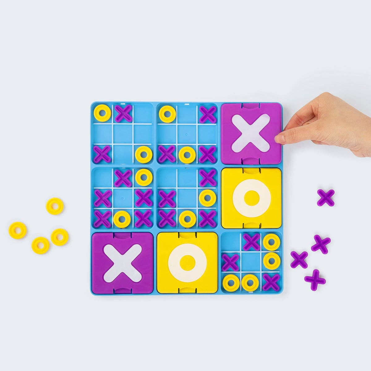 Colorful tic-tac-toe game board with hand placing a 'X' piece on a light gray background