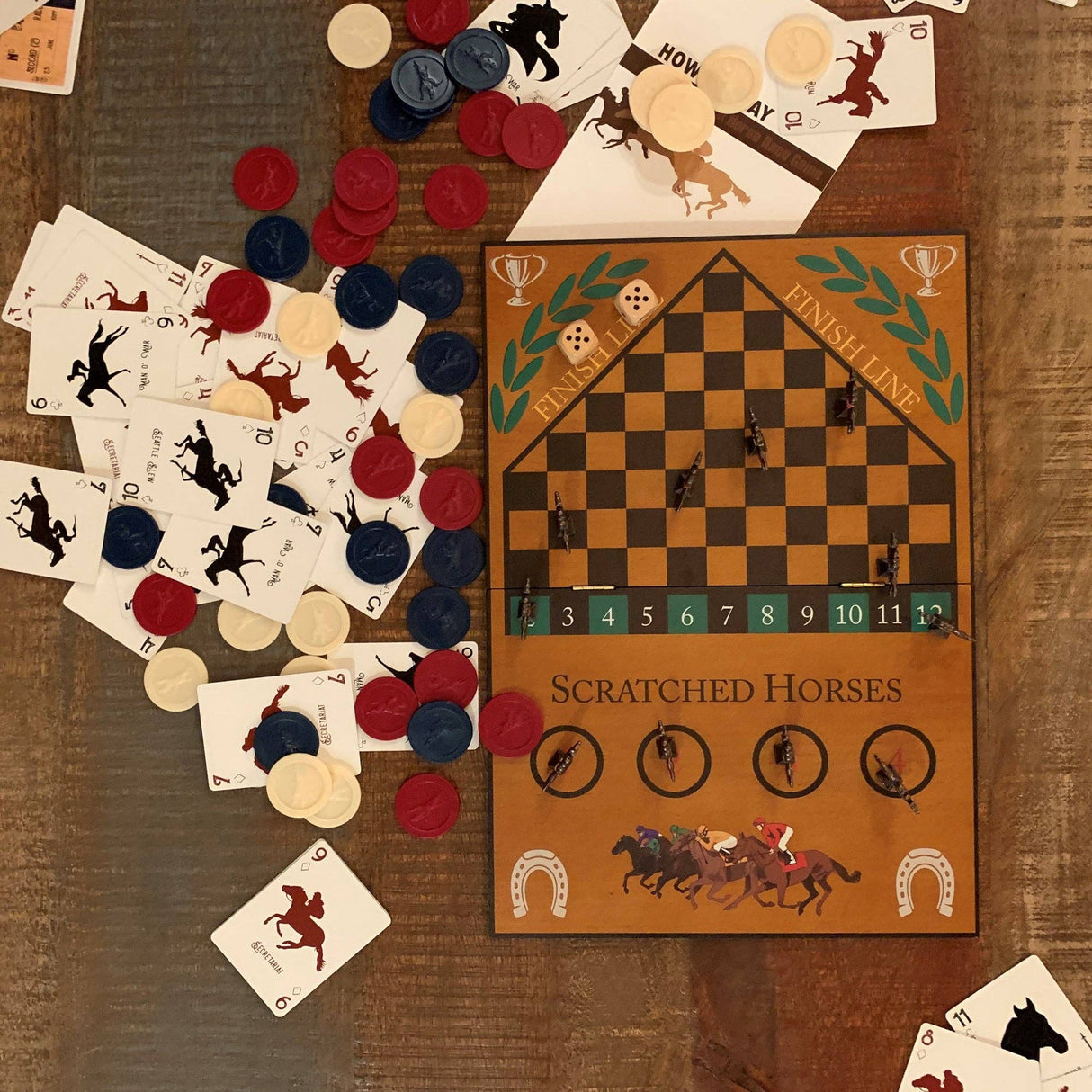 Board game with cards, chips, and a horse racing theme on a wooden surface.
