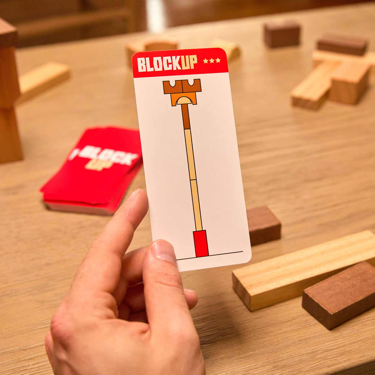 Hand holding a 'Blockup' card with wooden blocks on a table