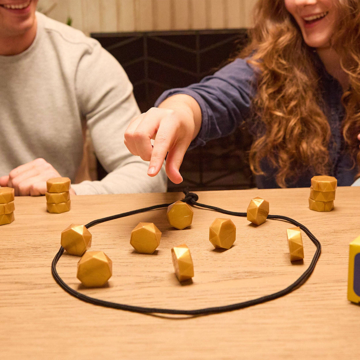 Two people playing a game with geometric wooden pieces on a table.
