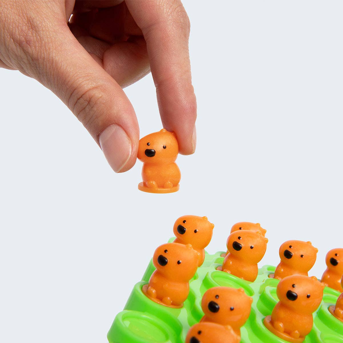 Hand interacting with a small orange bear figurine on a white background