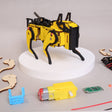 Yellow and black robotic arm model on a white platform with tools and parts on a gray surface