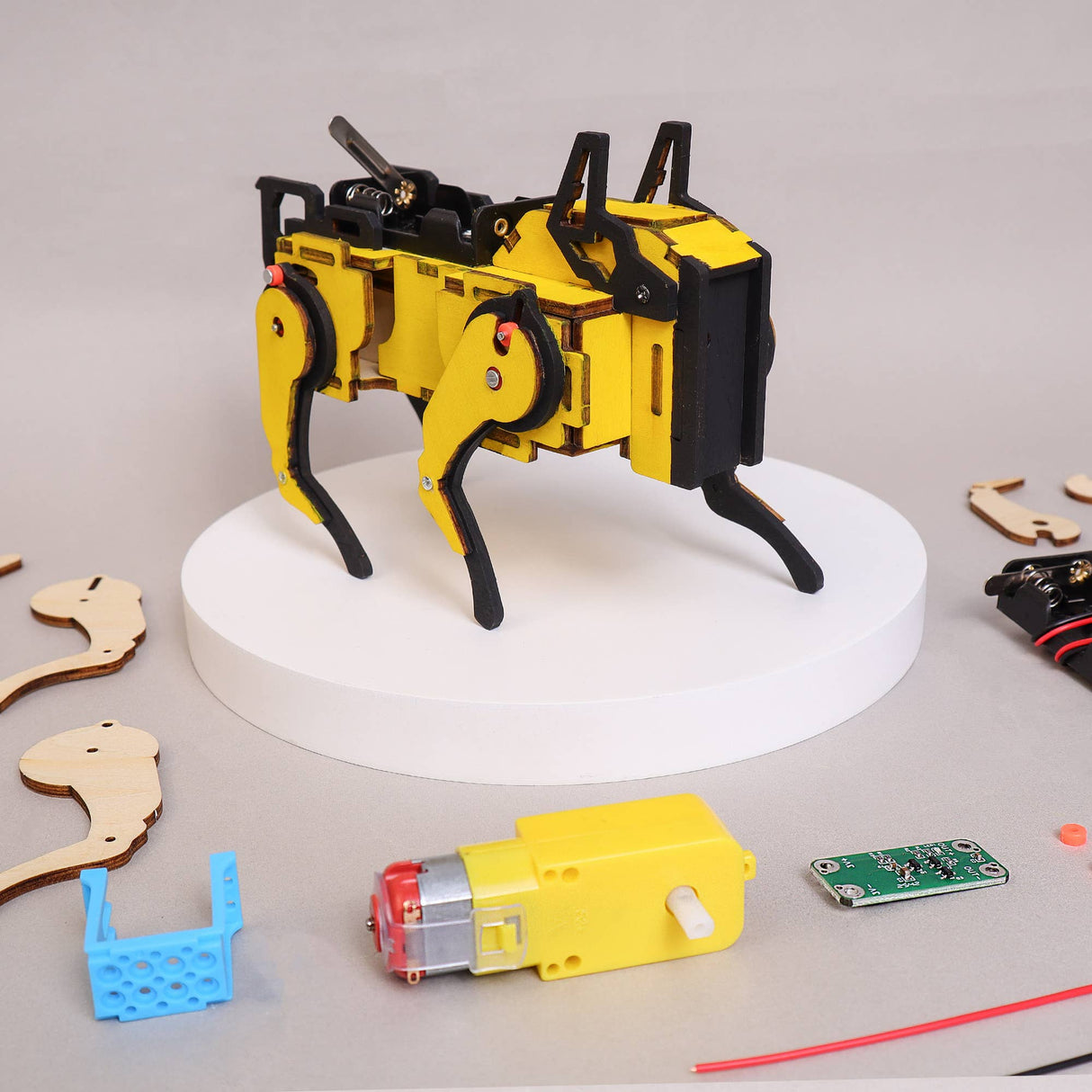 Yellow and black robotic arm model on a white platform with tools and parts on a gray surface