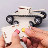 Hand holding a small control panel with buttons in front of a toy tank model.