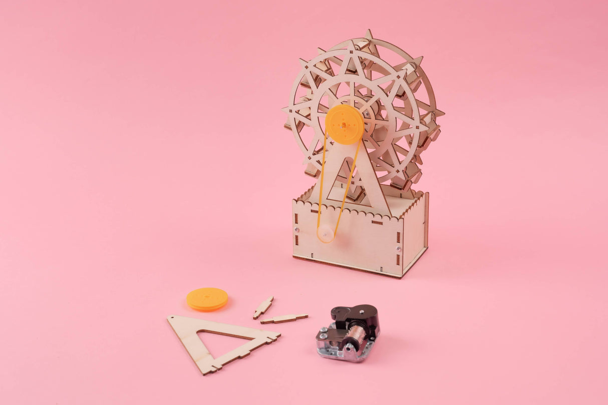 Wooden ferris wheel model with components on a pink background