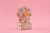 Wooden model of a Ferris wheel on a pink background