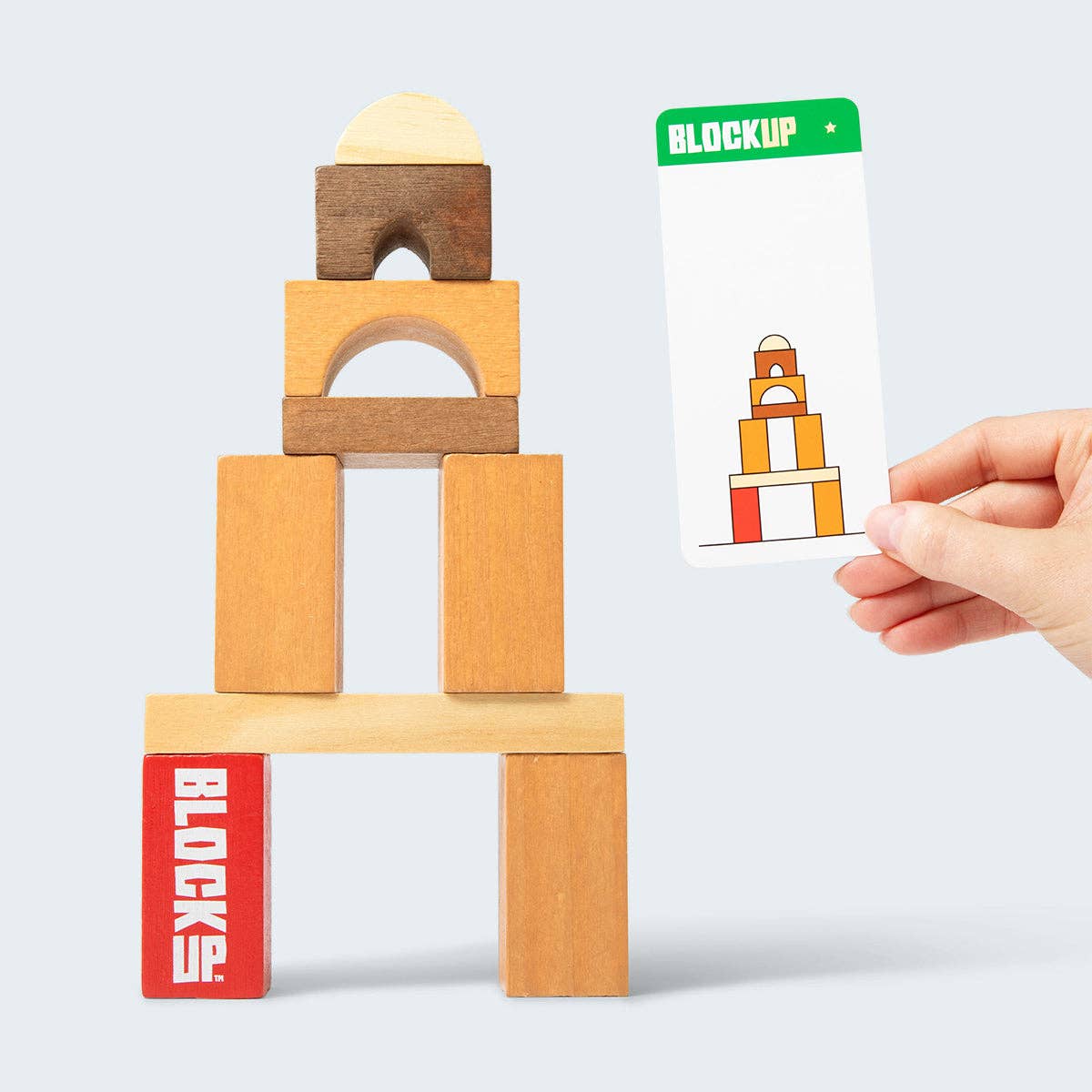 Wooden blocks stacked in a tower with a hand holding a card labeled 'BLOCKUP' against a white background.