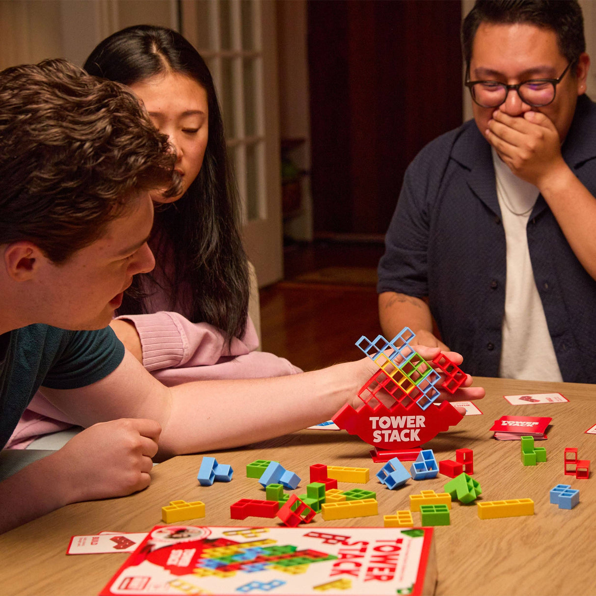 People playing a game of Tower Stack with colorful building blocks on a table.