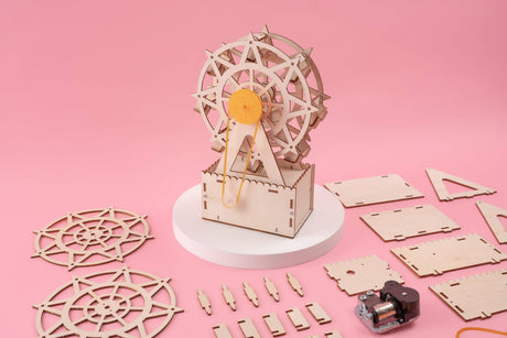 Wooden model kit of a Ferris wheel on a pink background