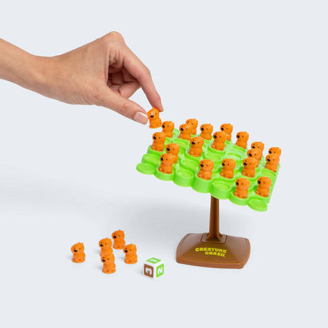 Hand placing orange game pieces on a green game board with 'Creature Cards' branding.